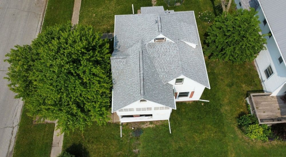 Aerial view of a white house with a gray roof surrounded by green trees and lawn.