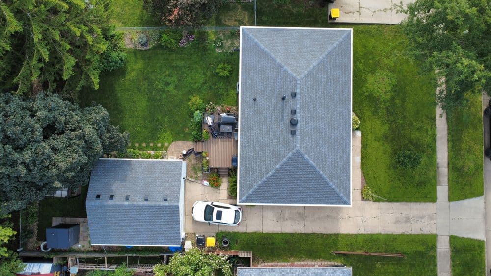 Aerial view of suburban home with landscaped yard and parked car in driveway.