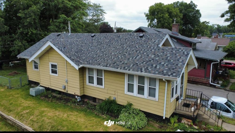 Aerial view of a yellow house with a shingled roof and green lawn.