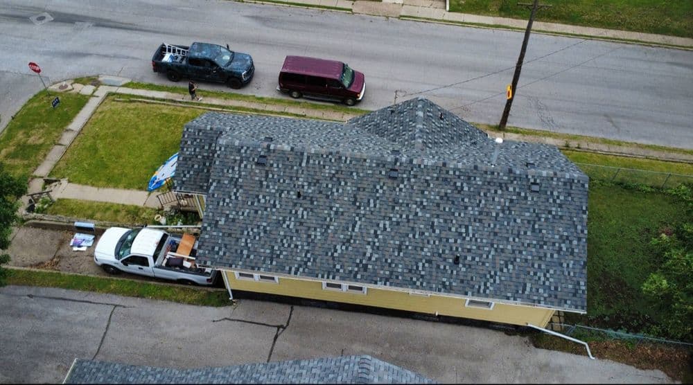 Aerial view of a yellow house with a gray roof, parked vehicles, and a suburban street.