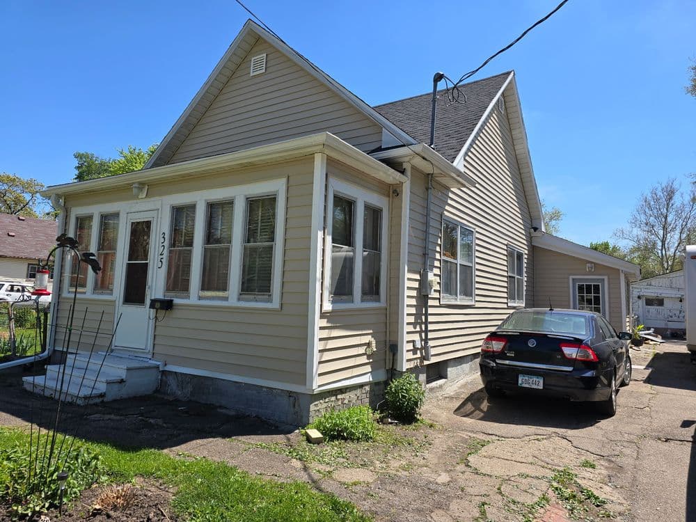 Front view of a light-colored single-family home with a car parked in the driveway.
