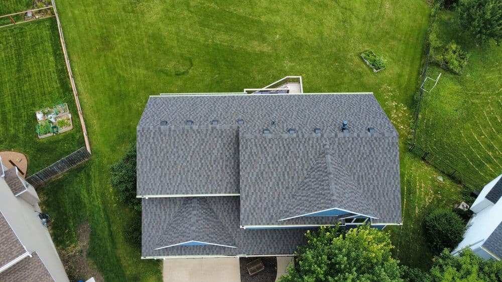 Aerial view of a residential roof with gray shingles and green lawn surrounding it.