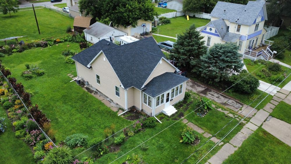 Aerial view of a charming home surrounded by lush gardens and green lawn in a residential area.