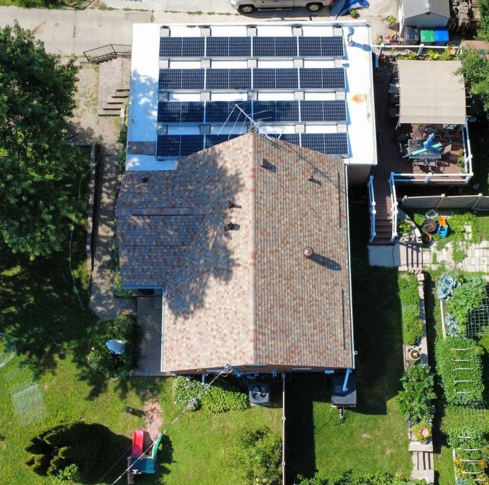 Aerial view of a house with solar panels on the roof and a green backyard garden.