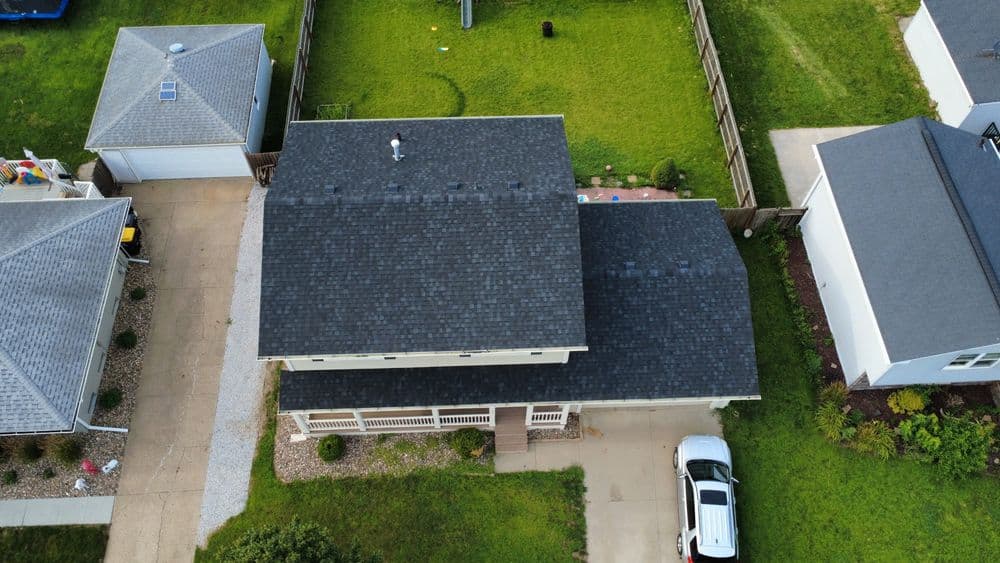 Aerial view of a residential home with a gray shingle roof and green lawn.