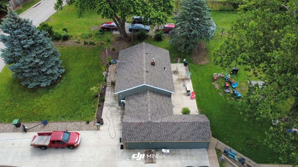 Aerial view of a residential house with a driveway, parked cars, and surrounding greenery.