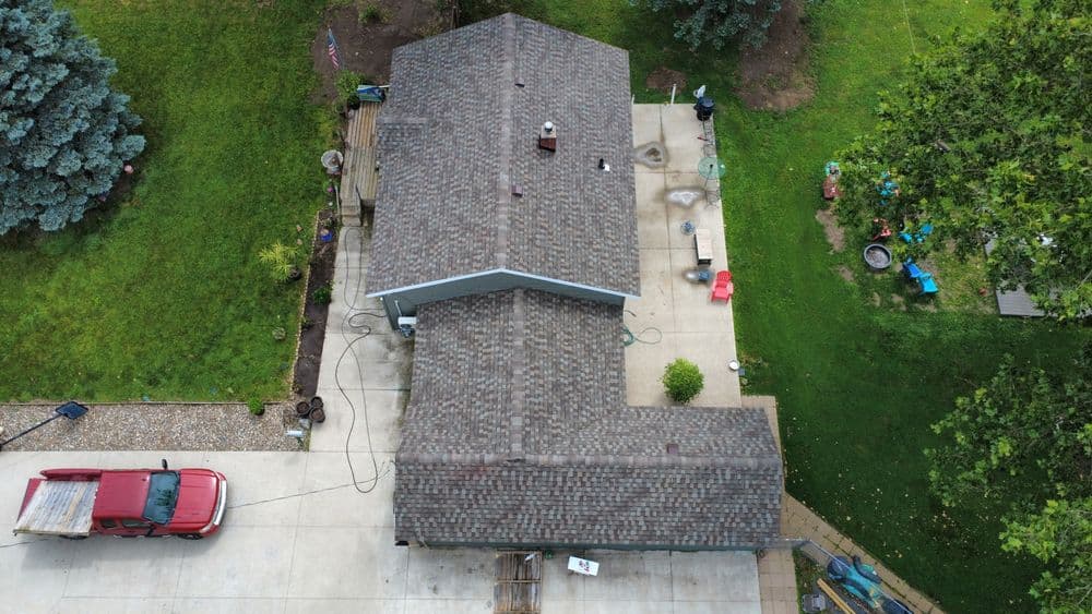Aerial view of a house with a textured roof, surrounded by a green lawn and trees.