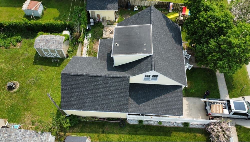 Aerial view of a house with a black roof surrounded by green lawns and outbuildings.