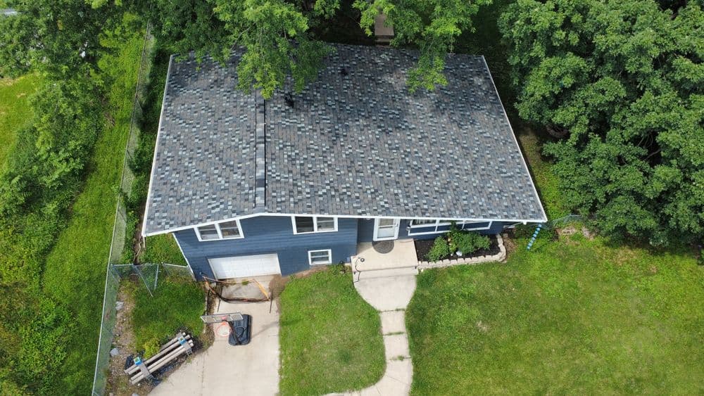 Aerial view of a blue house with a gray shingle roof surrounded by greenery.