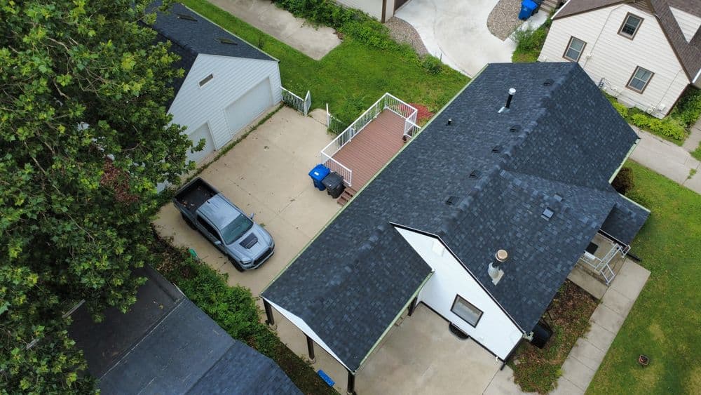 Aerial view of a suburban home with a gray car in the driveway and green lawn.