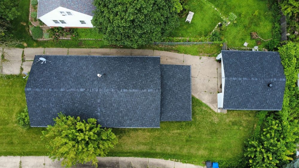 Aerial view of two houses with dark roofs and green lawns, showcasing their layout and surroundings.
