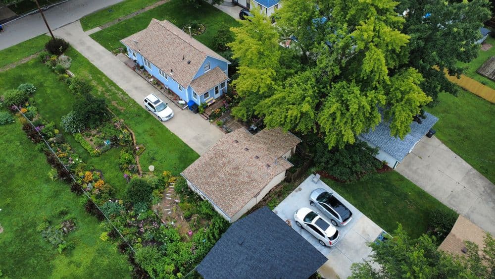 Aerial view of a suburban neighborhood featuring colorful gardens and three residential homes.