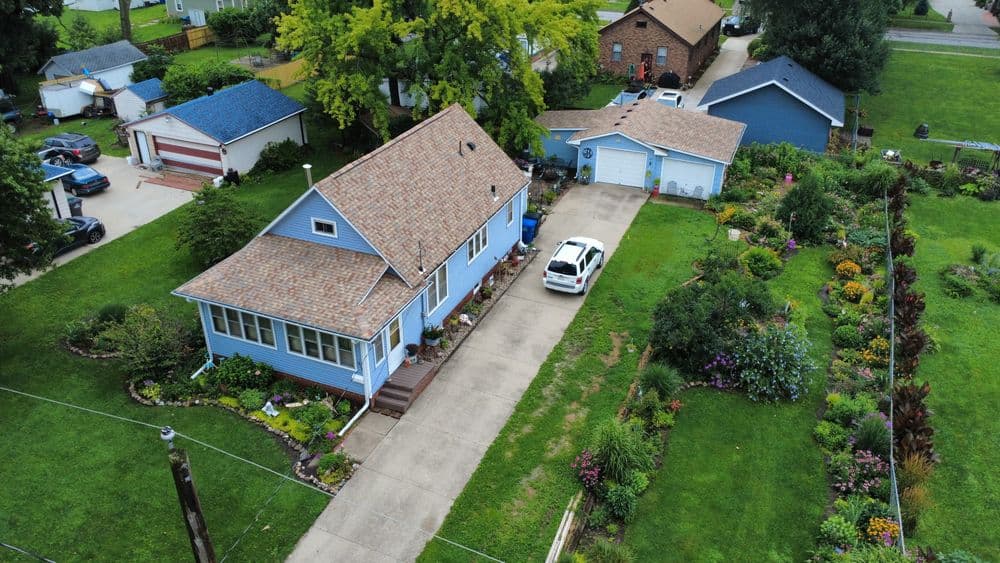 Aerial view of a blue house with a well-maintained garden and garage on a suburban street.