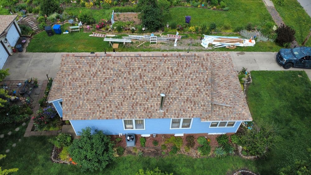 Aerial view of a blue house with a landscaped yard and garden, featuring a shingle roof.