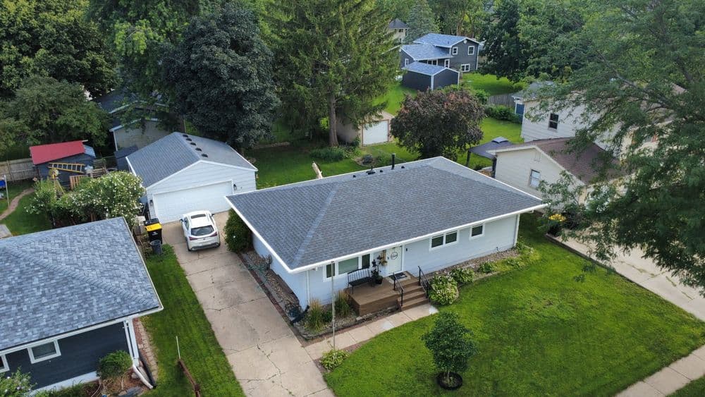 Aerial view of a suburban home with a gray roof surrounded by green grass and trees.