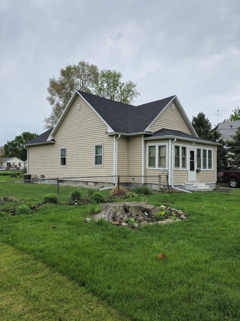 Charming beige house with a black roof and lush green yard, featuring a fence and garden.