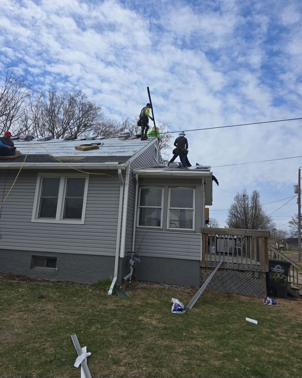 Workers installing a new roof on a house under a cloudy sky, with tools and safety gear visible.