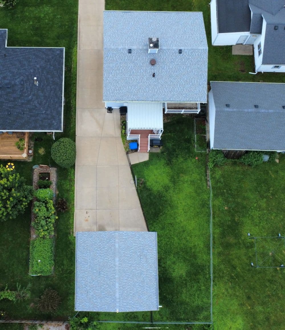 Aerial view of suburban homes with a paved driveway and green lawn areas.