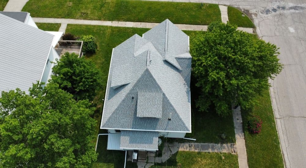 Aerial view of a house with a gray roof surrounded by greenery and sidewalk.
