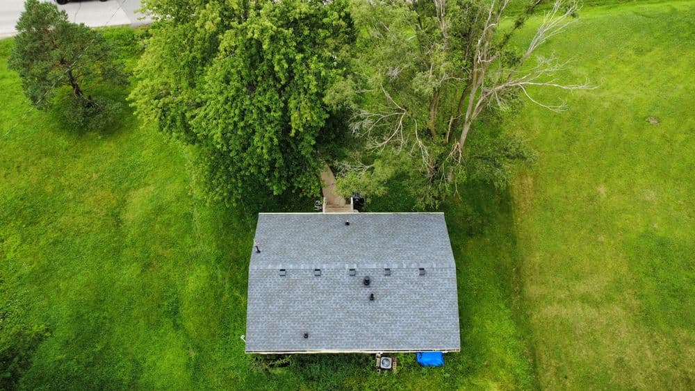 Aerial view of a house surrounded by lush greenery and trees on a sunny day.