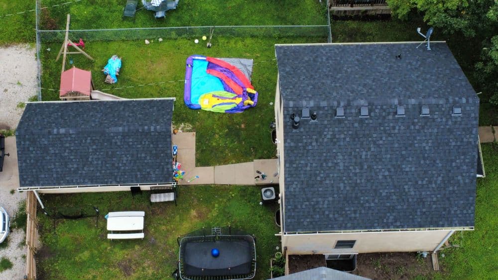 Aerial view of a backyard with colorful tarp, houses, and trampoline on a sunny day.