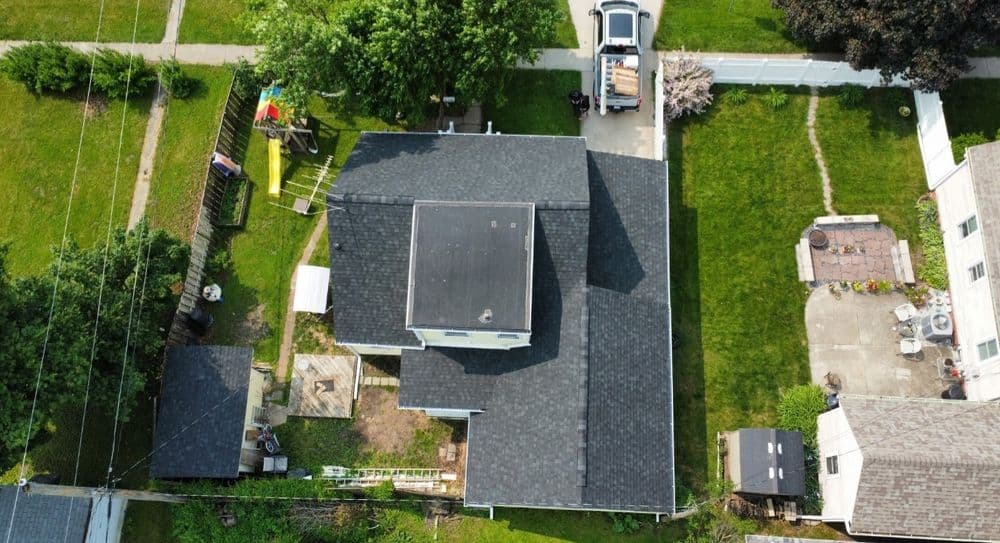 Aerial view of a residential home with a landscaped yard and nearby structures.