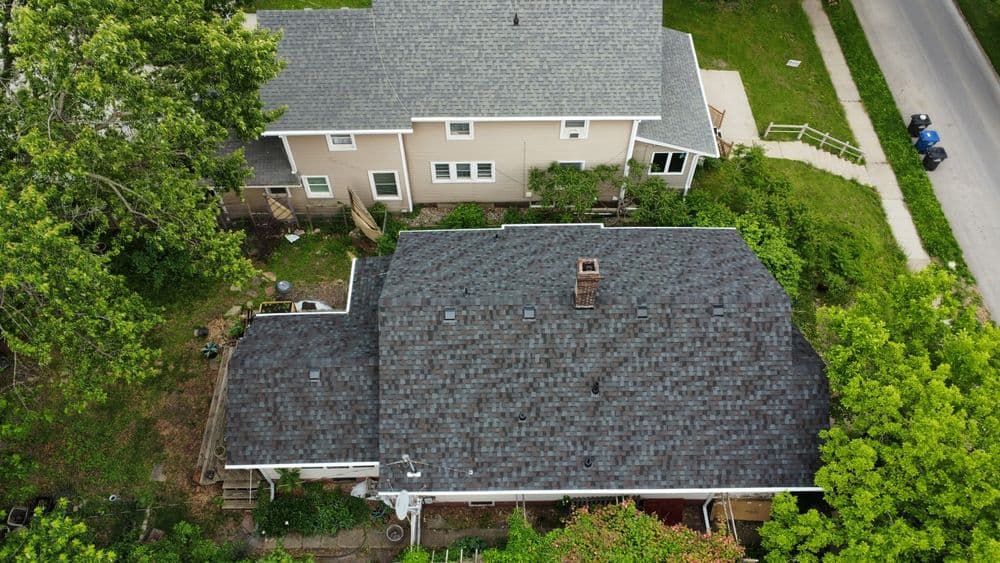 Aerial view of residential houses with asphalt shingle roofs and surrounding greenery.