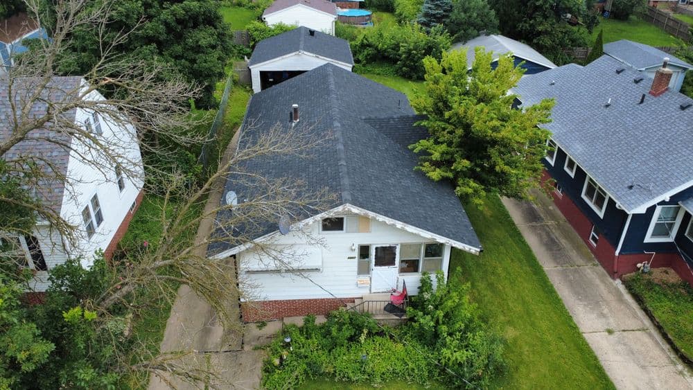 Aerial view of a house with a black roof surrounded by trees and greenery.