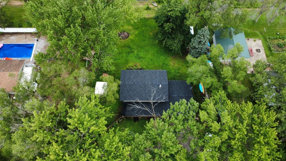 Aerial view of a home surrounded by lush greenery and trees, featuring a swimming pool nearby.