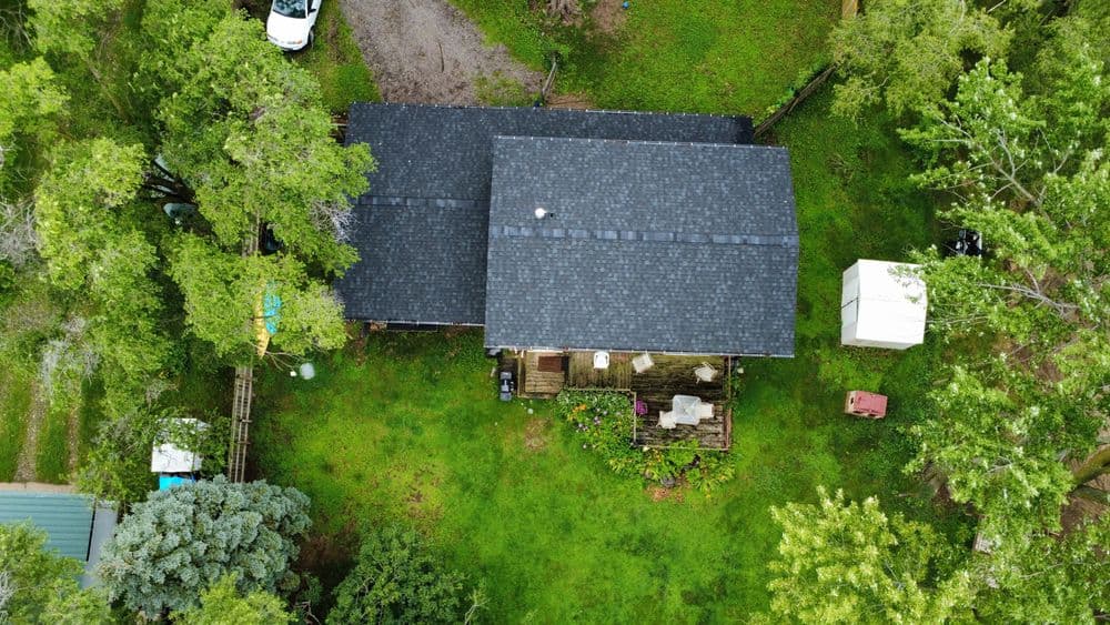 Aerial view of a house surrounded by greenery and trees on a sunny day.