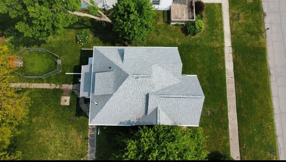 Aerial view of a house with a gray roof surrounded by green lawns and trees.