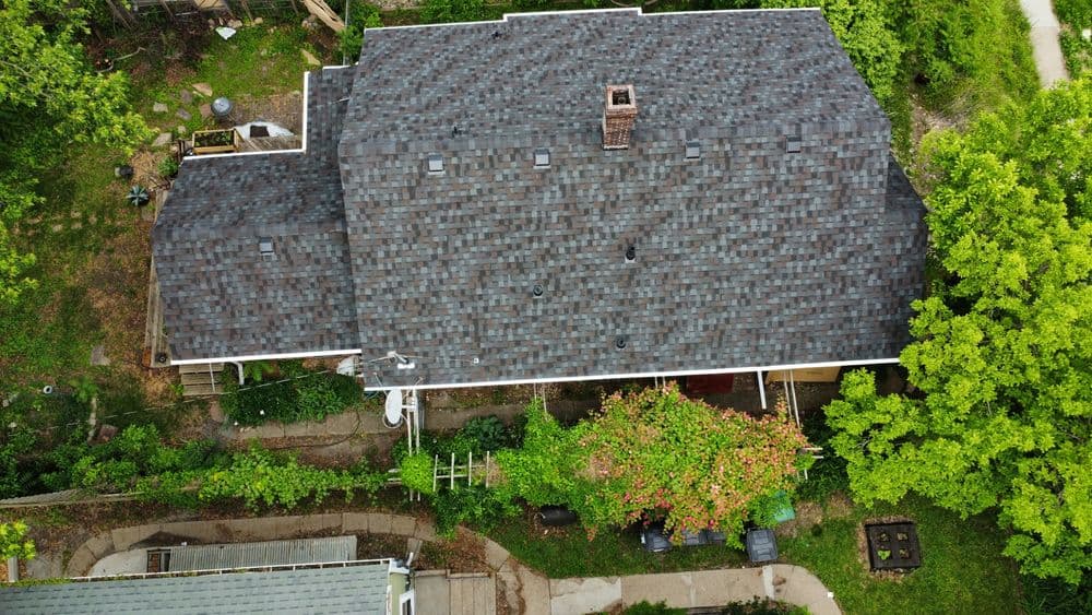 Aerial view of a house with a dark shingle roof surrounded by lush greenery and pathways.