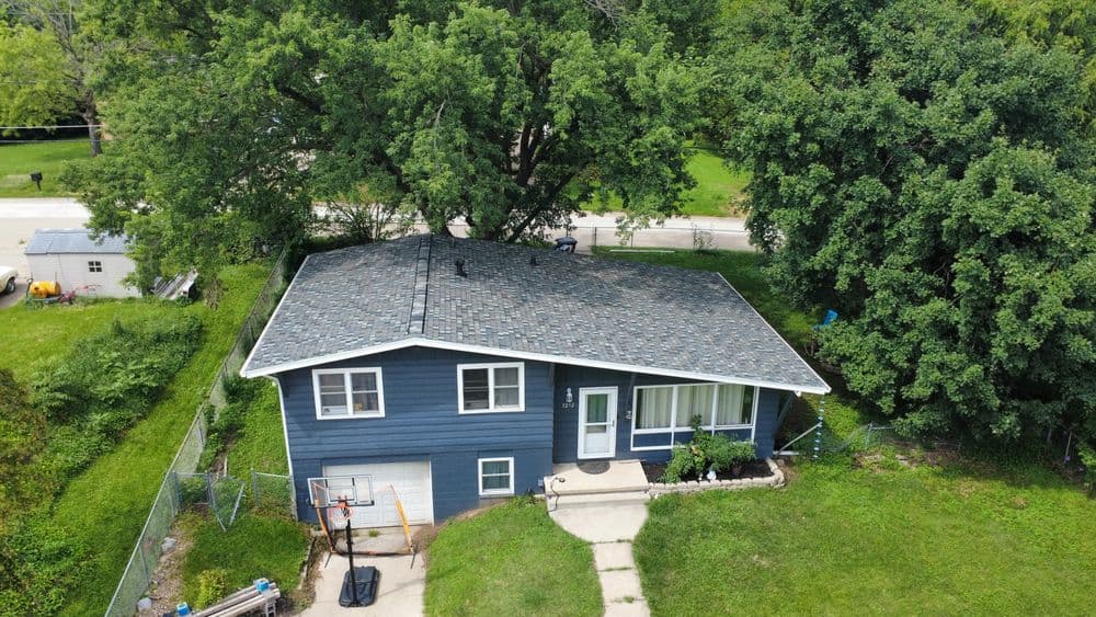 Aerial view of a blue house with a sloped roof, basketball hoop, and green lawn.