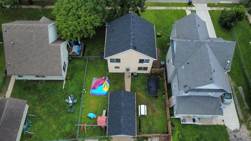 Aerial view of suburban homes with backyard play area and inflatable water slide on green lawn.