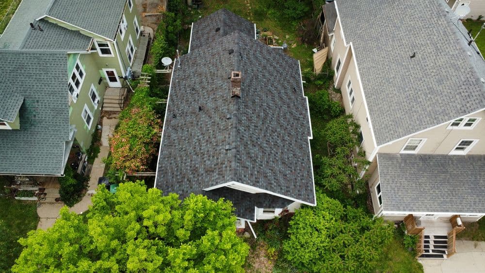 Aerial view of residential roofs surrounded by greenery and neighboring houses.