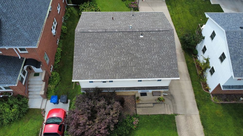 Aerial view of a suburban home with a gray roof, red car, and landscaped yard.