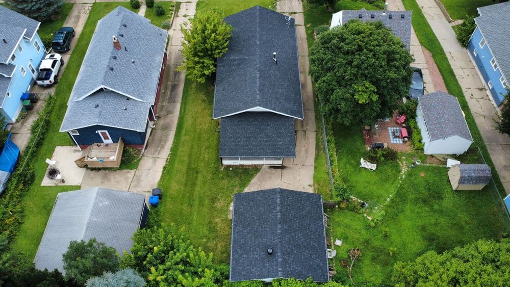 Aerial view of residential neighborhood with houses, green lawns, and tree-lined yards.