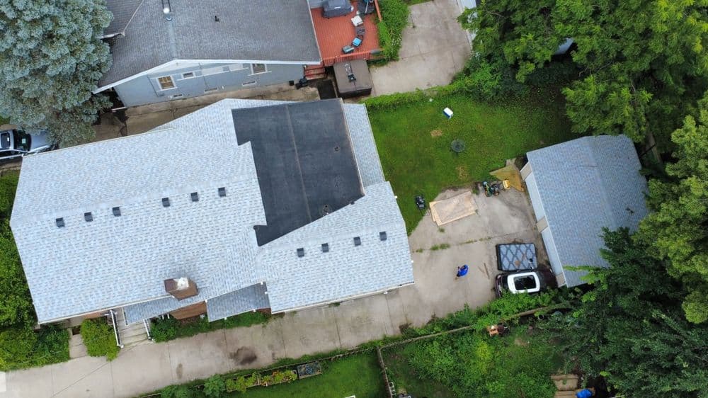 Aerial view of houses with gray roofs and green lawns, showcasing landscaping and nearby vehicles.