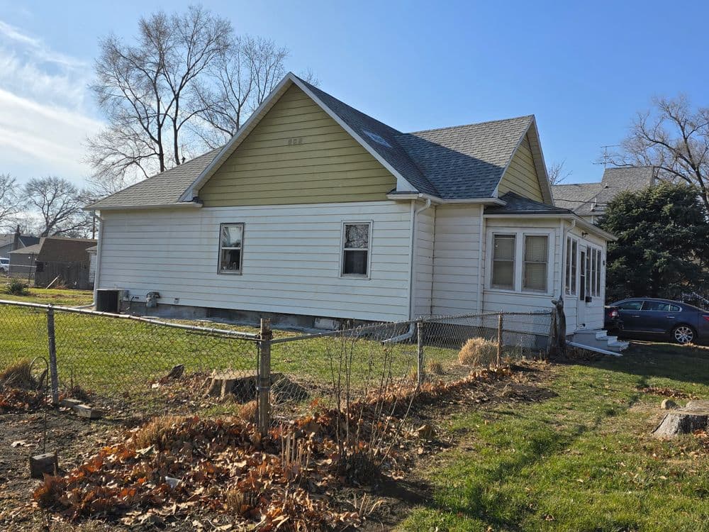 White-sided house with yellow accents, fenced yard, and clear blue sky in the background.