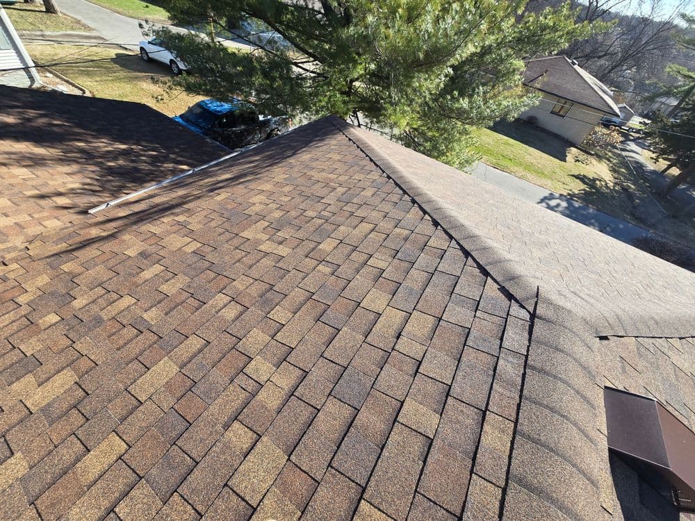 Aerial view of a textured brown shingle roof on a residential home with trees and roads nearby.