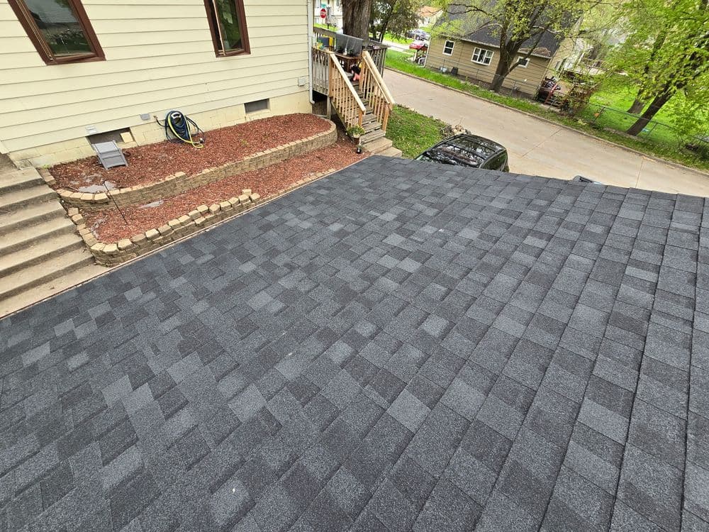 Aerial view of a newly shingled gray roof with surrounding landscaping and steps.