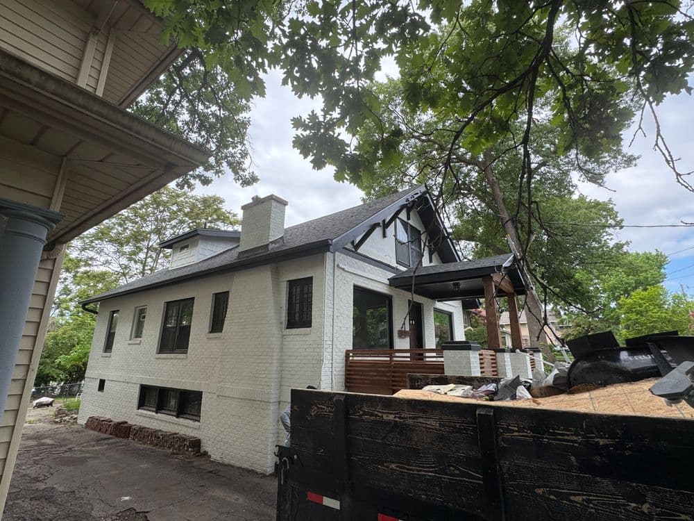 Renovated home with a new roof, surrounded by trees and construction materials.