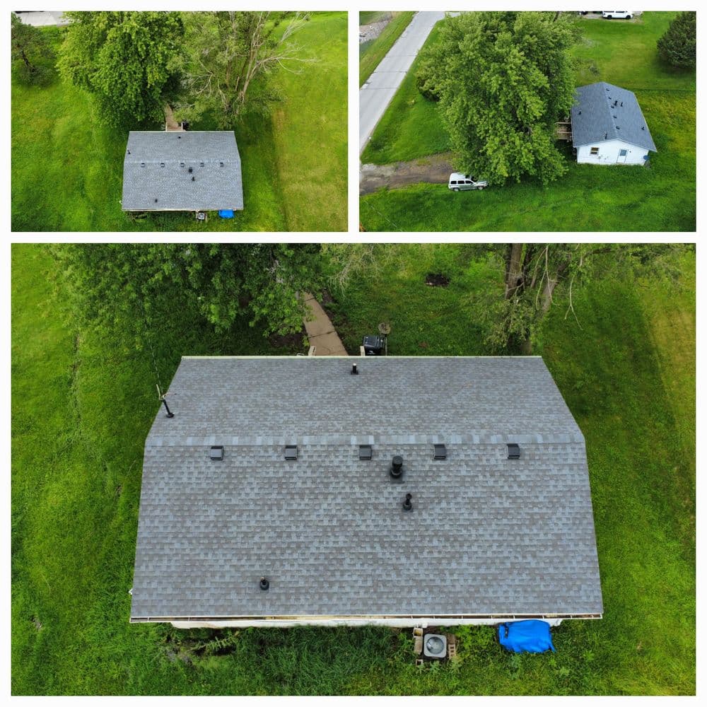 Aerial view of a house with a gray roof, surrounded by green grass and trees.