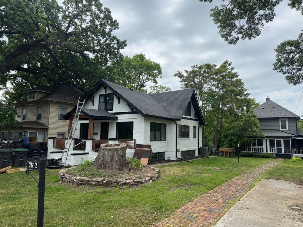 Renovated white house with black trim and landscaping, featuring a ladder and nearby homes.